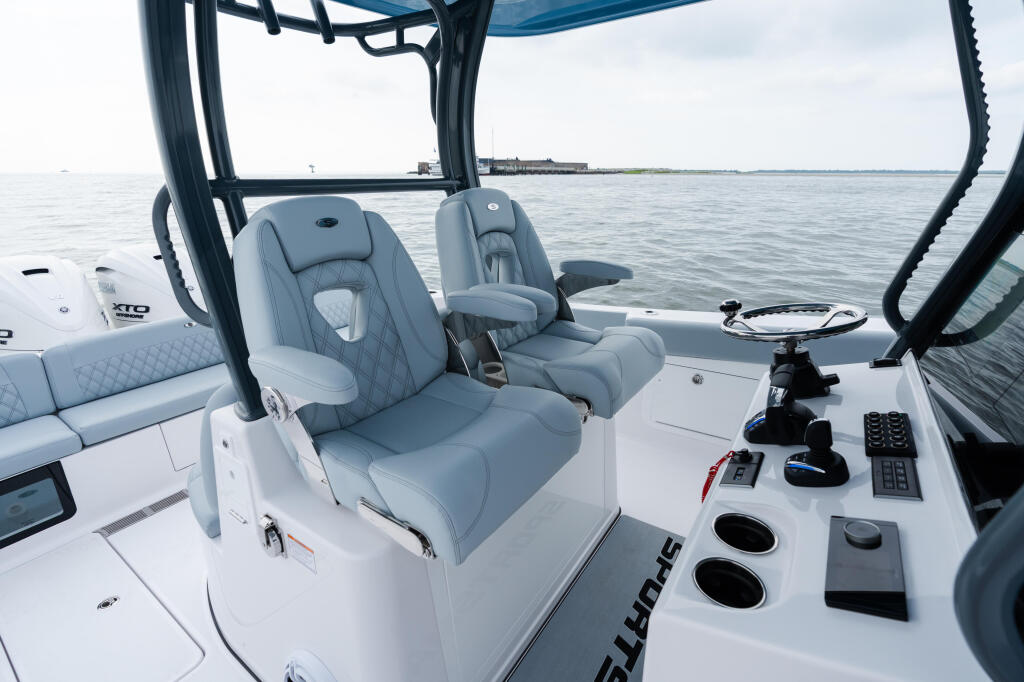 Helm station with gray upholstered captain's chairs and control panel under black hard-top canopy, open water visible beyond