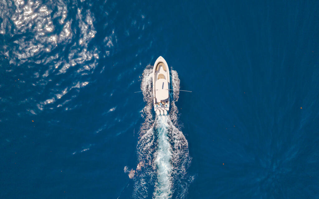White sport fishing boat cutting through deep blue offshore waters, aerial view from above