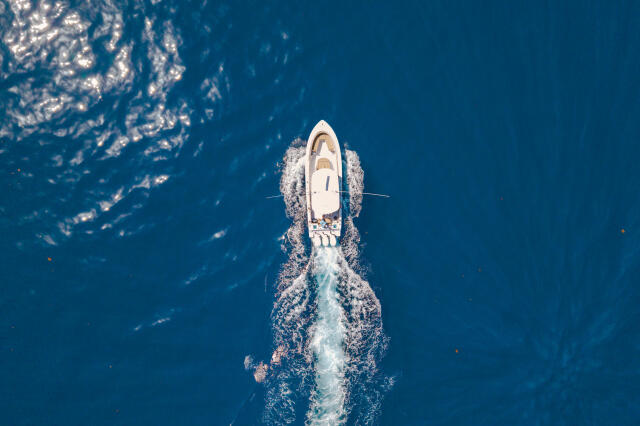 White sport fishing boat cutting through deep blue offshore waters, aerial view from above