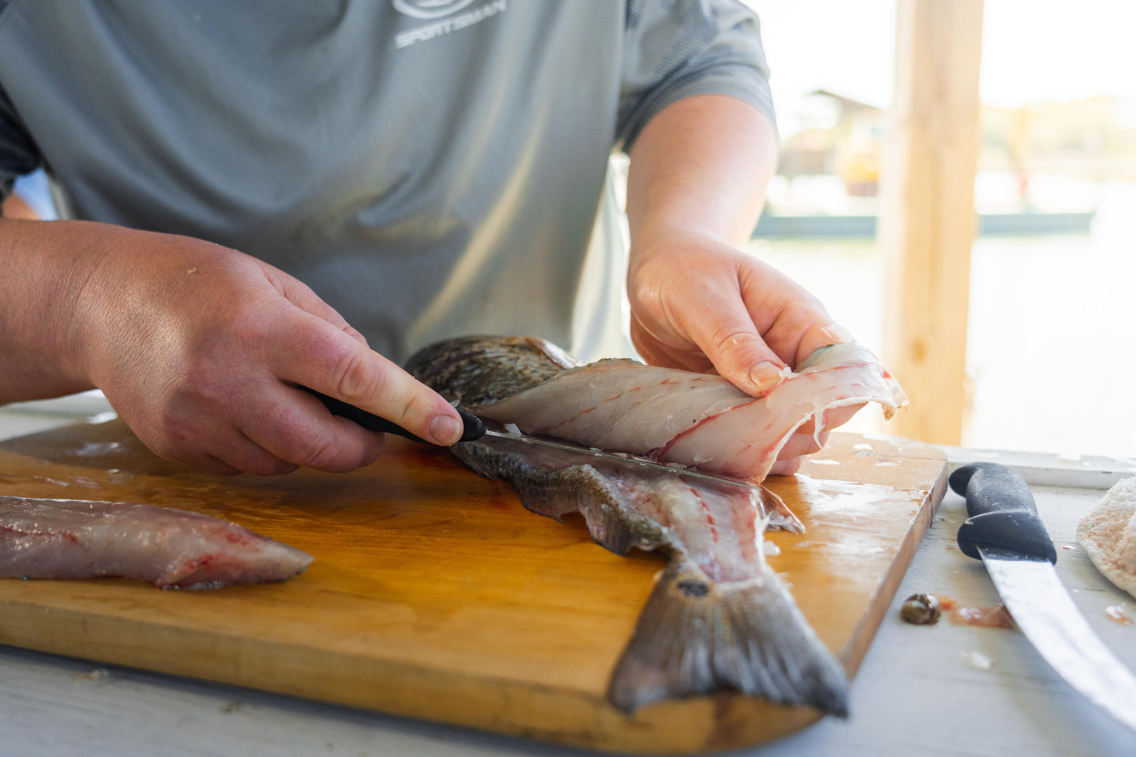 A person fillets a fresh redfish on a wooden cutting board with a knife nearby
