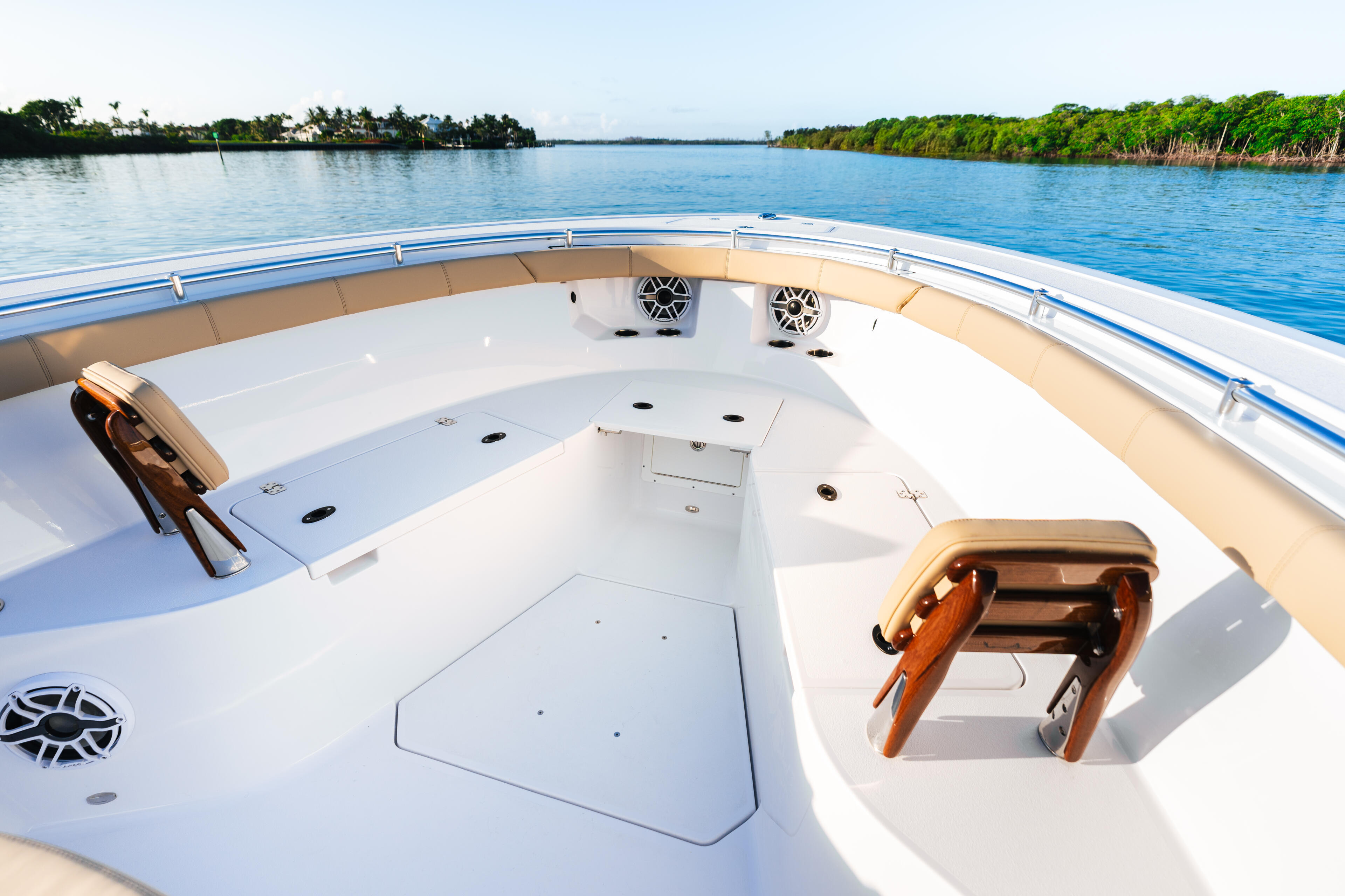 Spacious bow seating and open deck area on a white sport boat with calm blue water and mangrove shoreline ahead