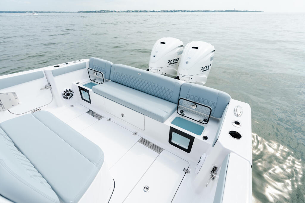 Aerial view of a white center console boat with dual outboard engines, gray upholstered seating, and electronics display in calm shallow water