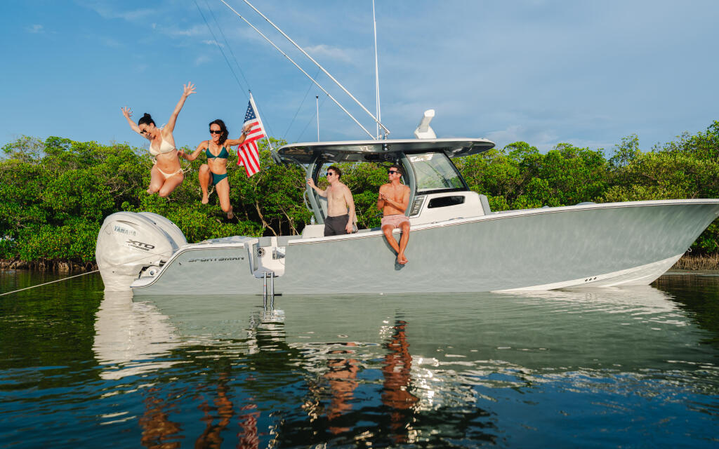 Group of friends enjoying a boat day in mangrove waters, with two jumping off the swim platform