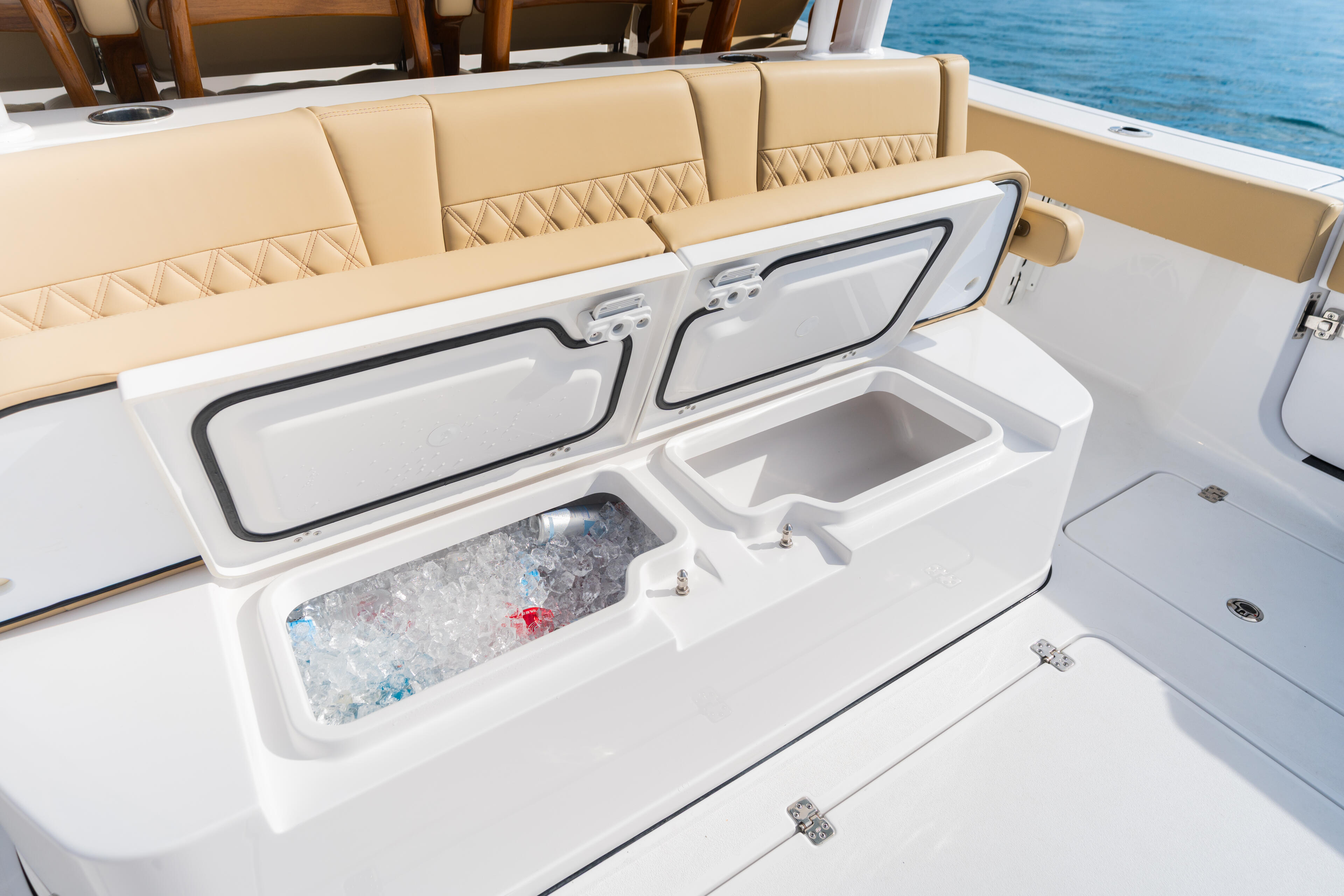 Open cooler with ice and drinks next to cushioned seating on boat cockpit overlooking blue water