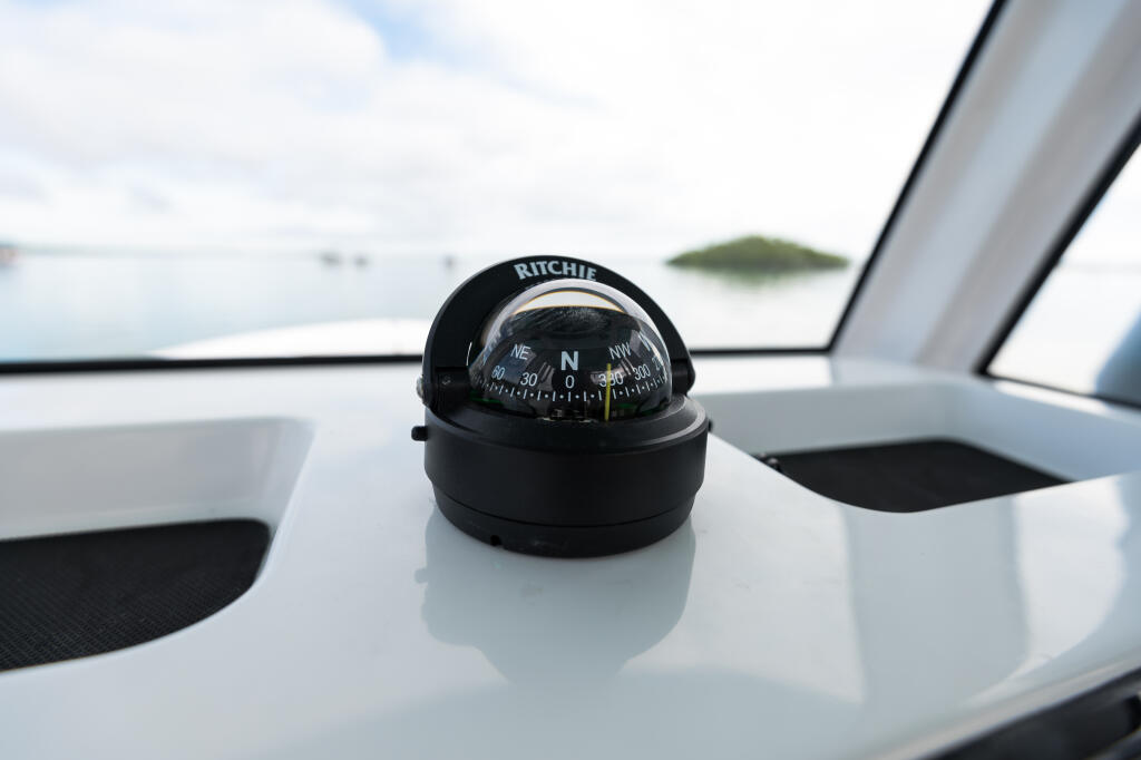 Ritchie compass mounted on the white helm console with calm water and distant island visible through the windshield