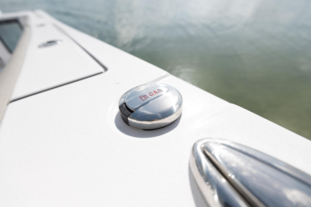 Dual fuel cap and chrome cleat detail on white boat gunwale above calm water