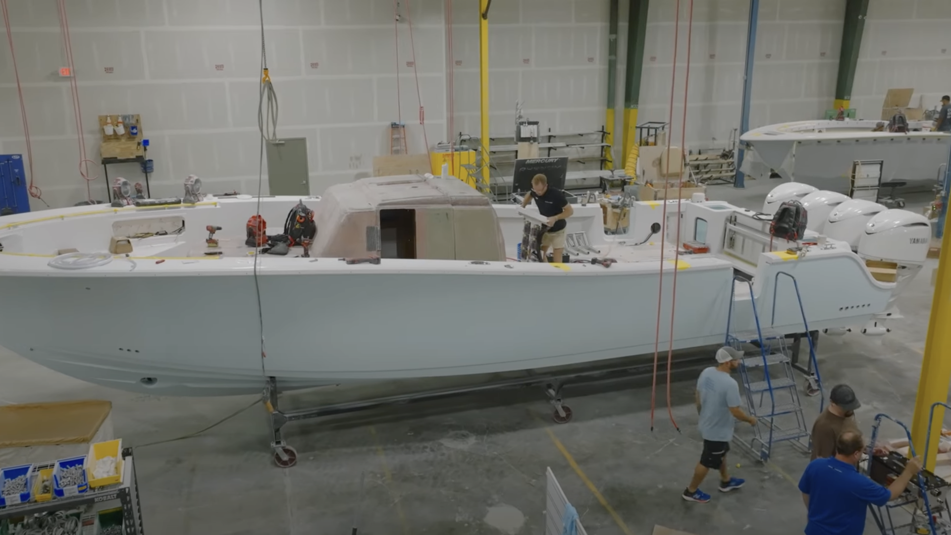 Boat under construction in a manufacturing facility with workers on scaffolding and ladders