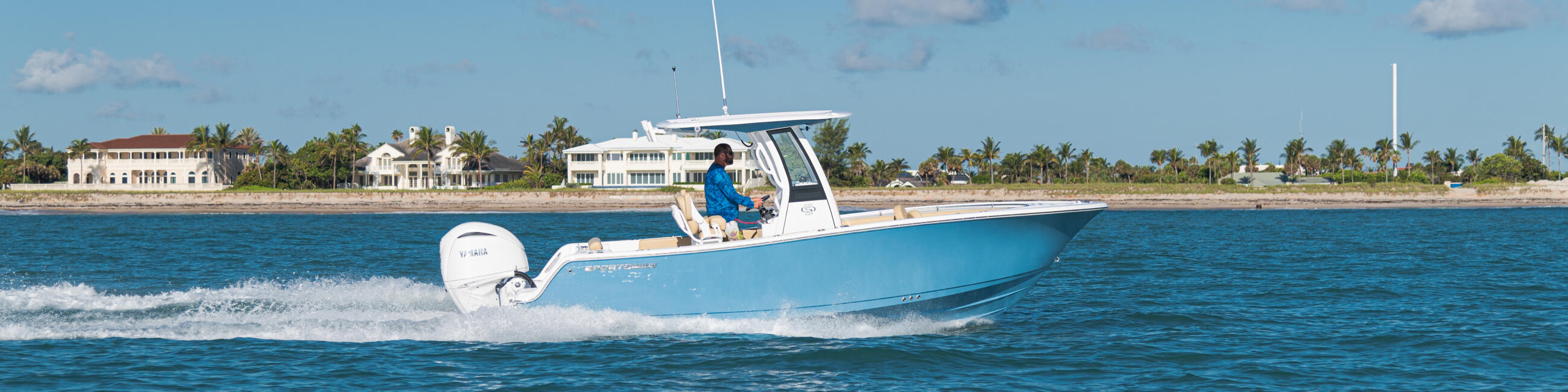 Blue and white center console boat running offshore with operator at helm, palm-lined beach visible in background