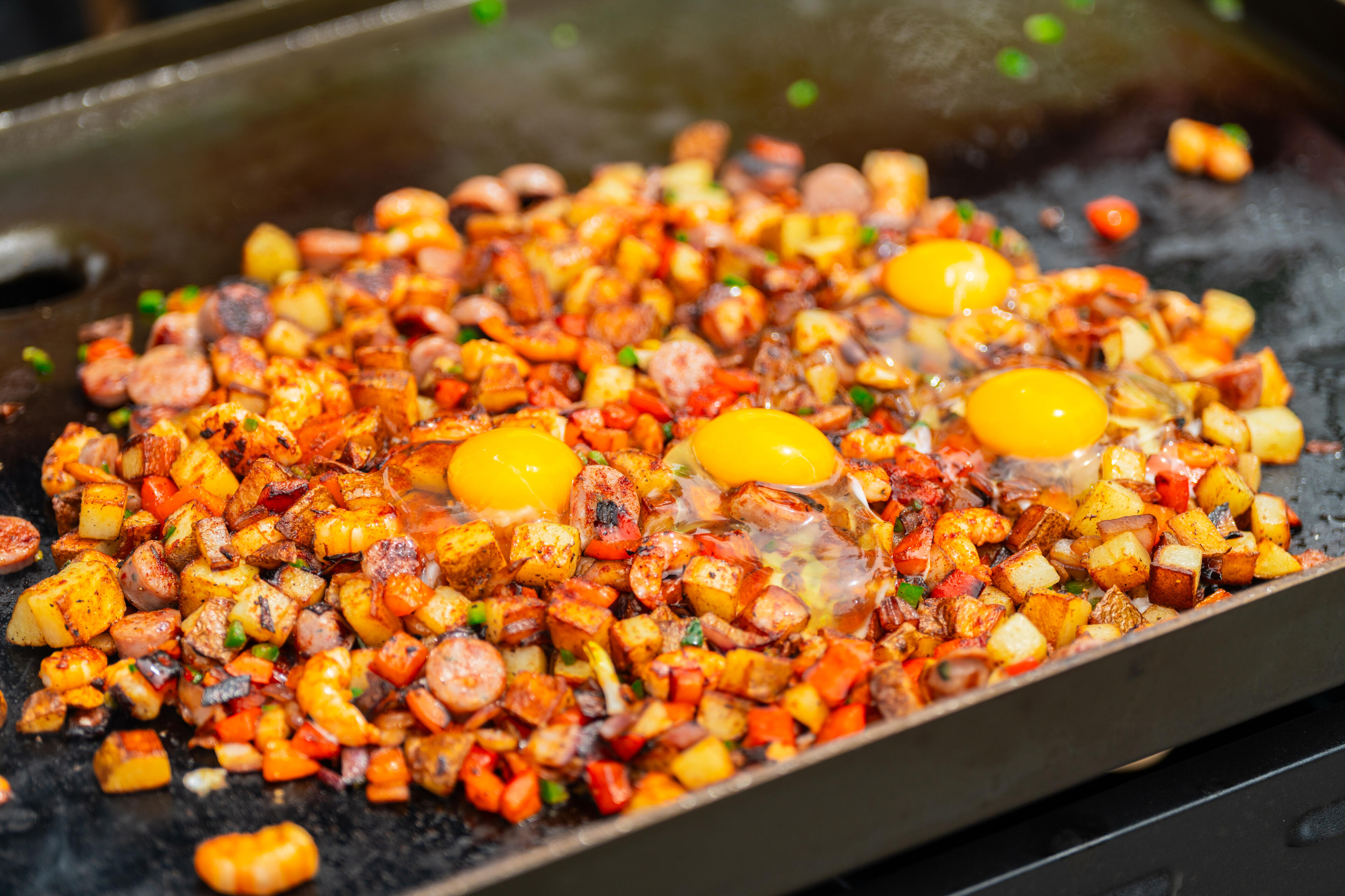 Lowcountry hash cooking on a flat griddle with sausage, potatoes, corn and eggs