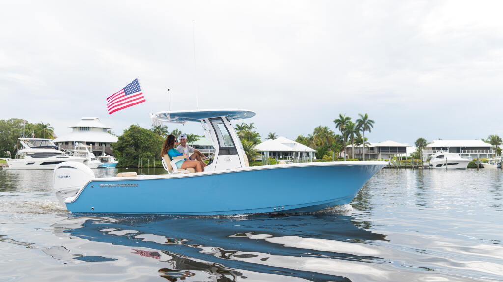 Couple relaxing on a blue and white center console boat anchored in shallow water with palm trees and waterfront homes visible behind