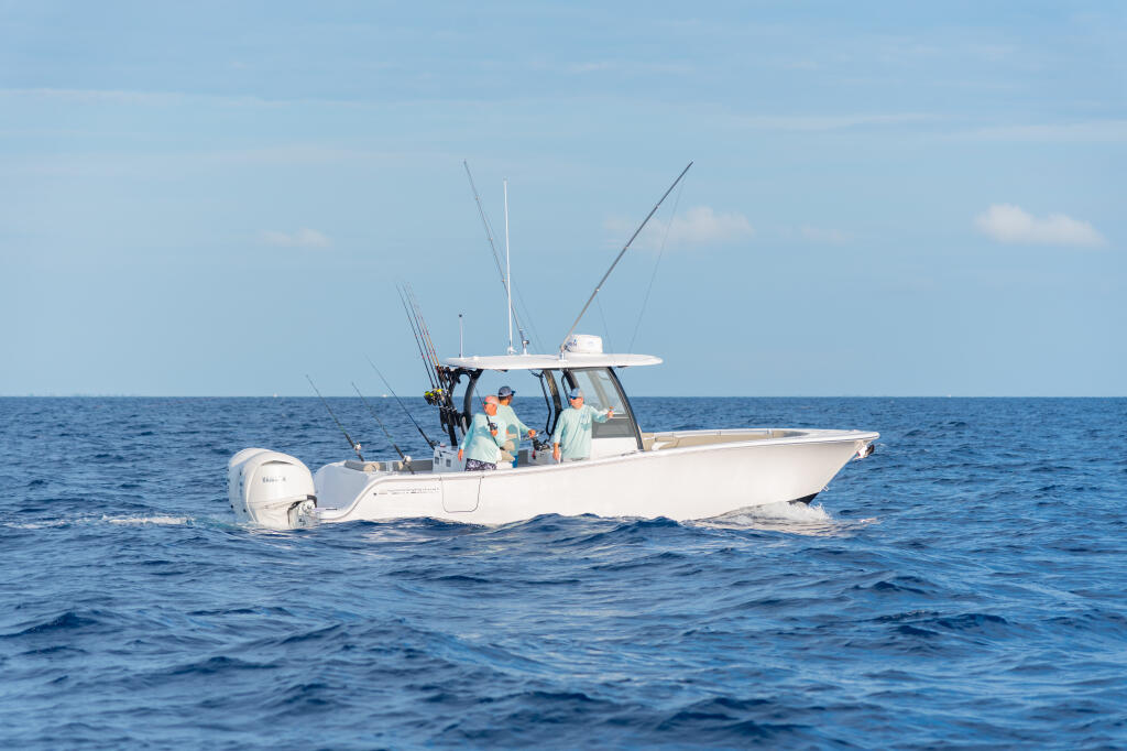 White offshore fishing boat with multiple anglers and fishing rods running in calm blue water