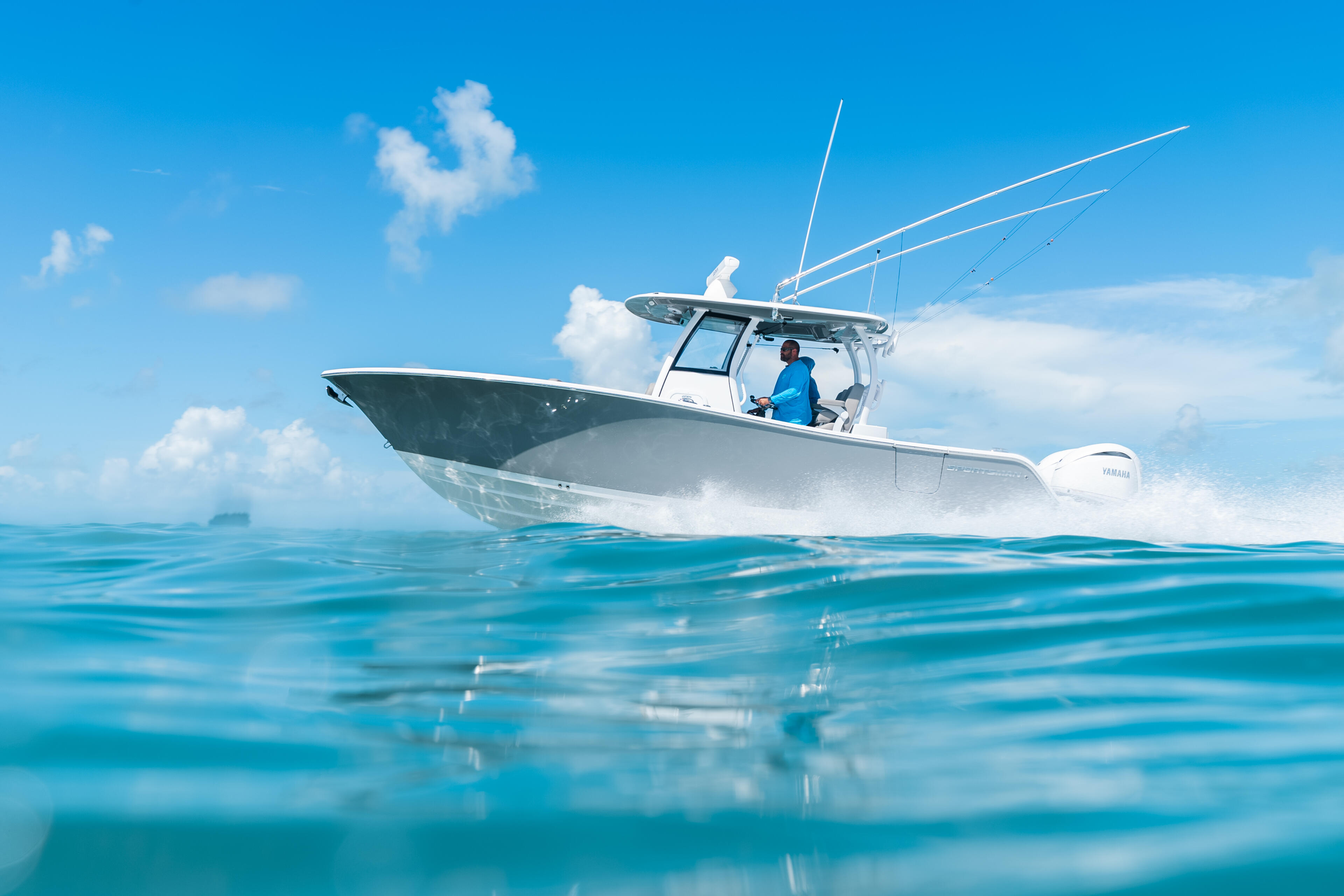 Fishing boat running at speed through turquoise offshore waters with operator at helm under clear sky