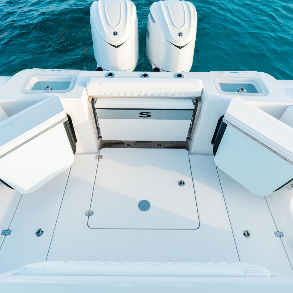 Overhead view of a center console boat's cockpit with side-entry doors, dual engines, and storage compartments on turquoise water