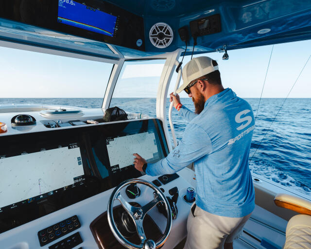 Angler at helm of offshore fishing boat monitoring fish finder screens while cruising open water
