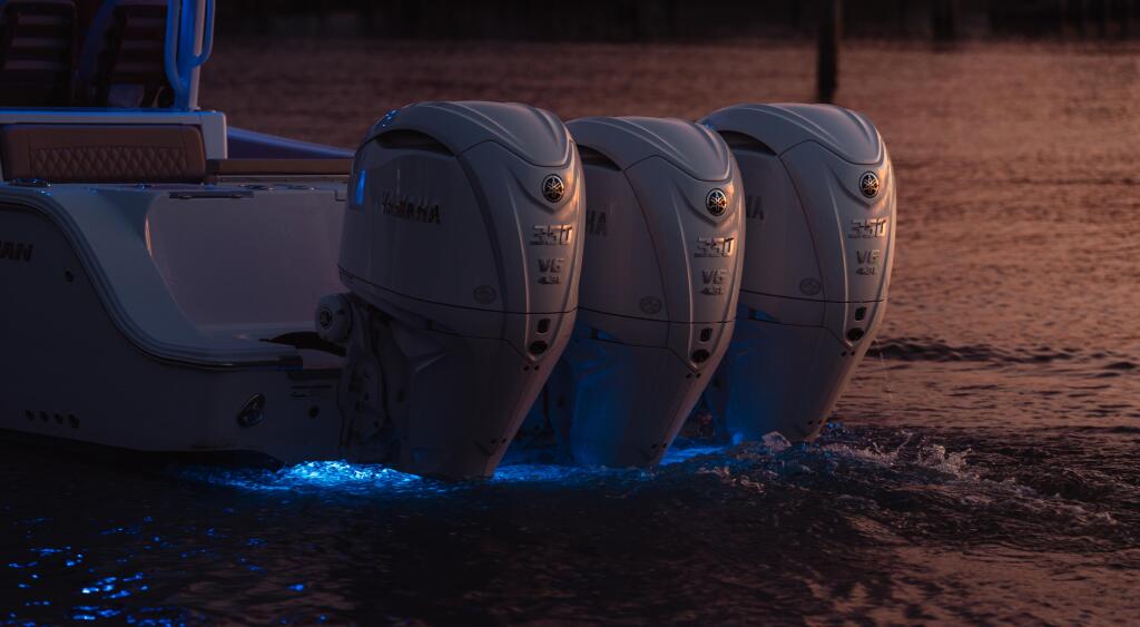 Three outboard engines mounted on a boat at dusk with bioluminescent water glowing blue beneath the hull