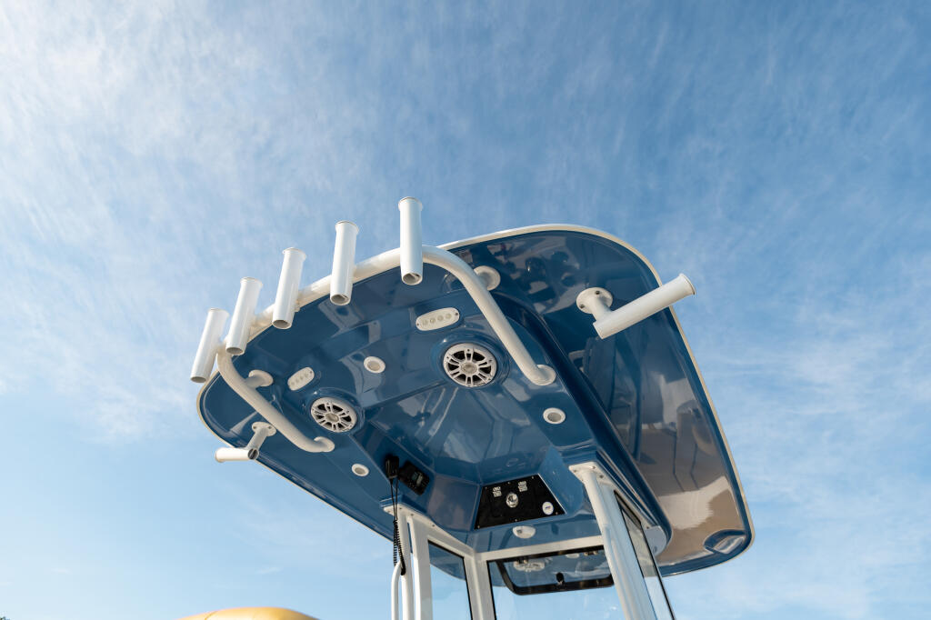 Overhead view of a center console boat's hard-top canopy with white railings and integrated lighting fixtures against blue sky
