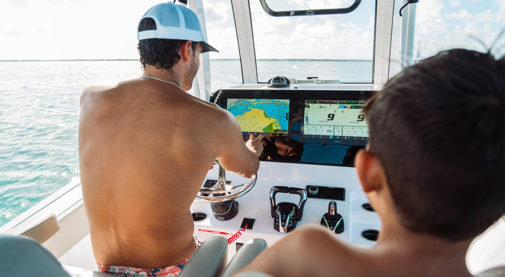 Captain monitoring GPS and fishfinder displays while navigating offshore in calm shallow waters