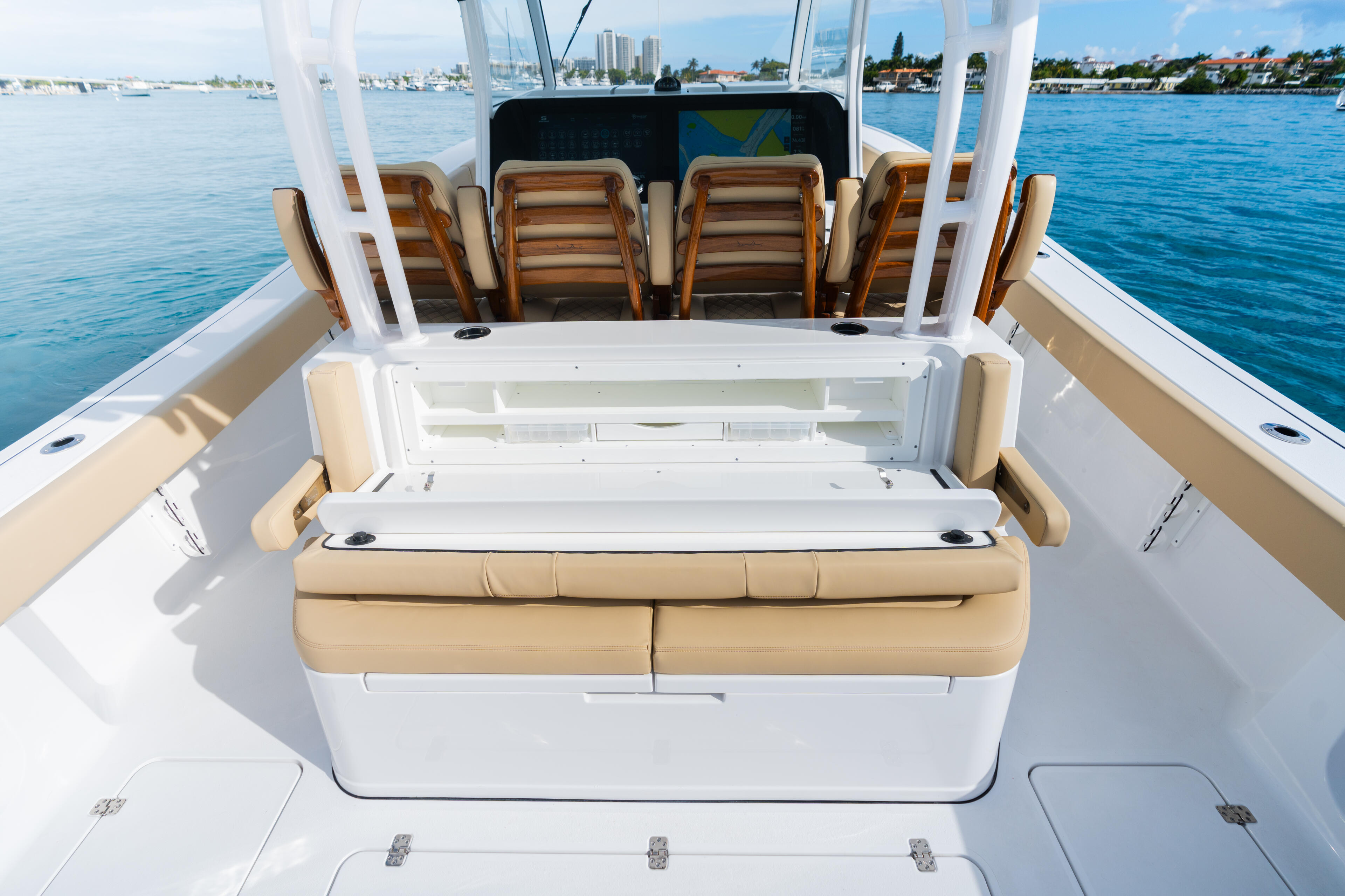Open cockpit with tan cushioned seating, white hard-top frame, and flip-down storage bench overlooking a marina and blue water