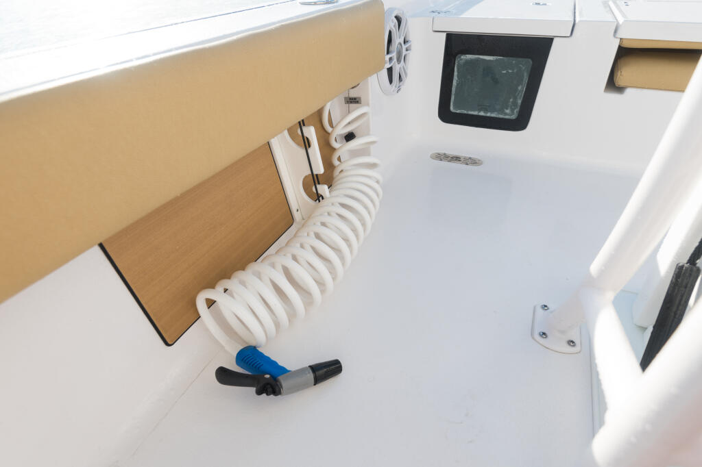 Boat helm area with raw water washdown system, white coiled hose, and electronics display mounted on the console