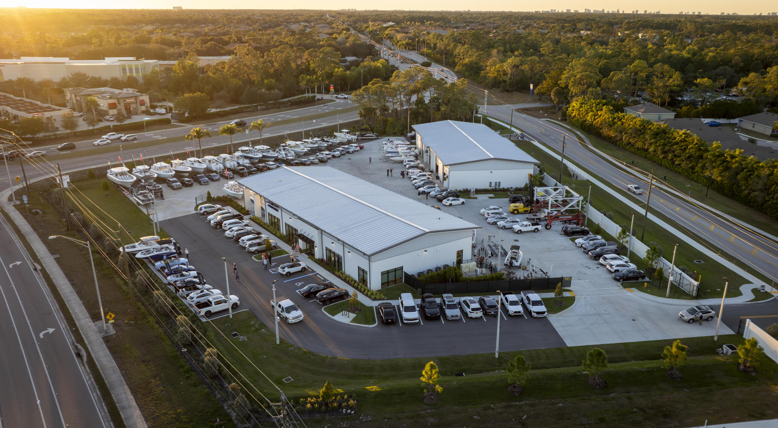 Aerial view of a boat dealership with multiple vessels in the yard and service buildings at sunset