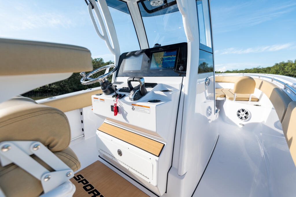 Center console helm area with dual monitors, steering wheel, and tan upholstered seating overlooking open water
