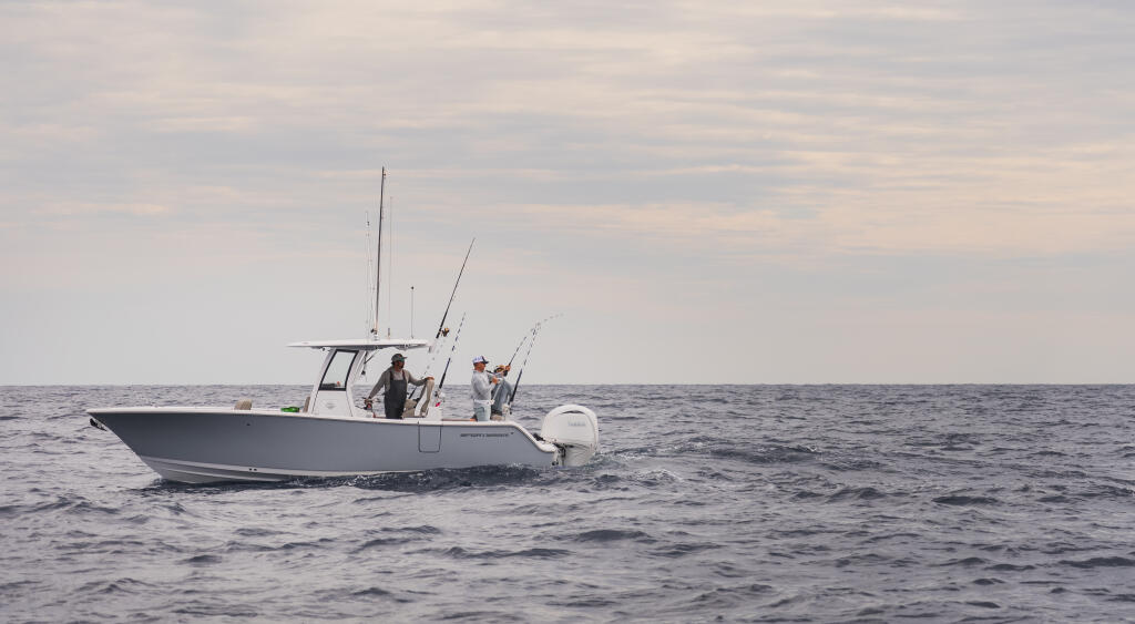 Fishing boat with multiple anglers and fishing rods deployed, running offshore in calm waters