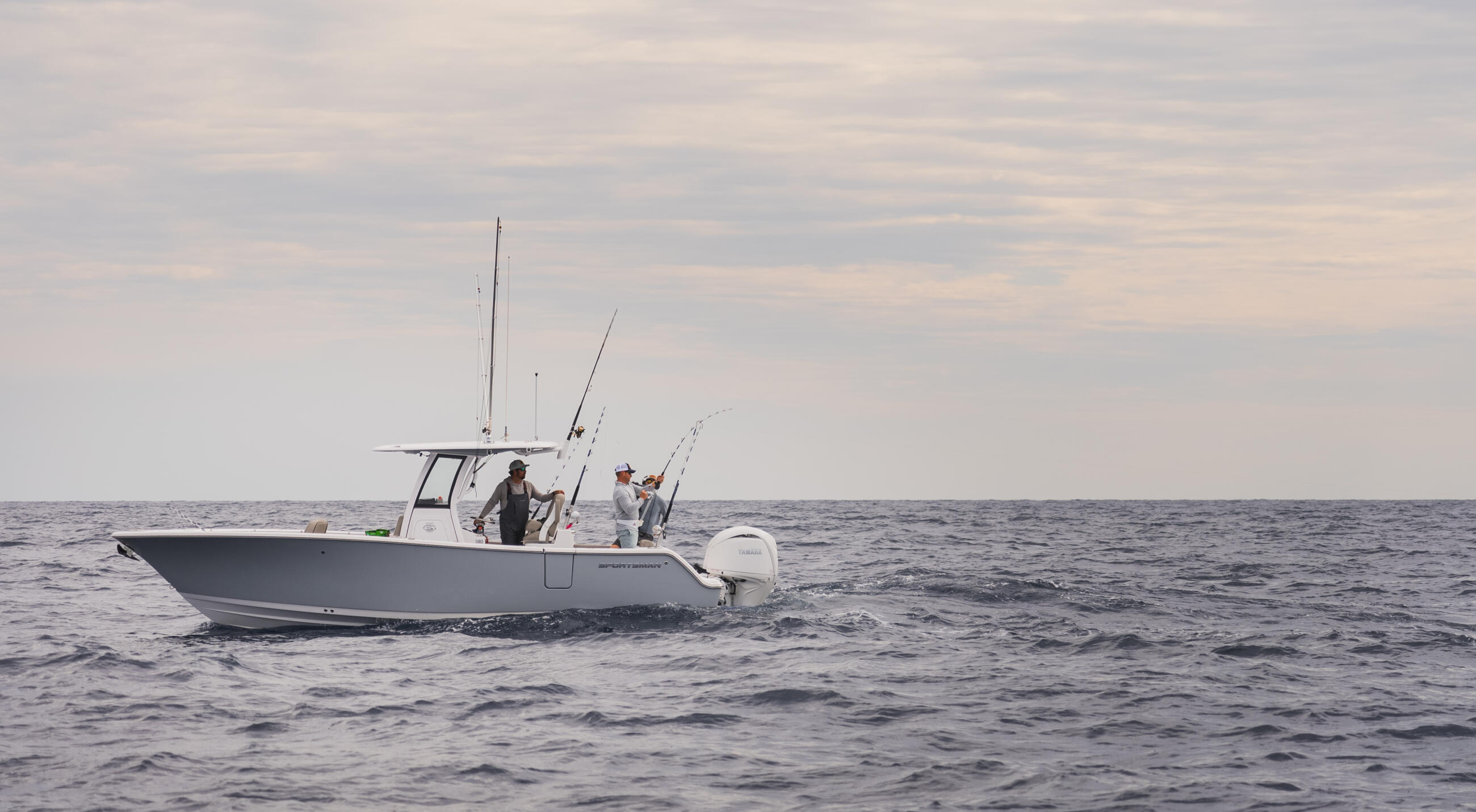 Fishing boat with multiple anglers and fishing rods deployed, running offshore in calm waters