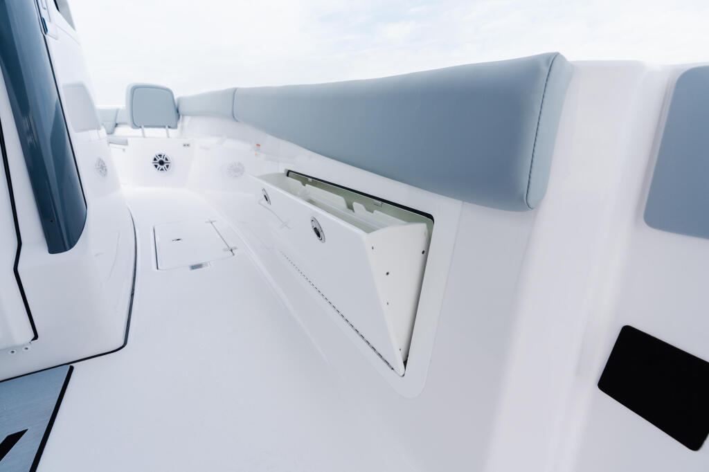 Boat deck with gray upholstered seating, storage compartment, and helm area under clear sky