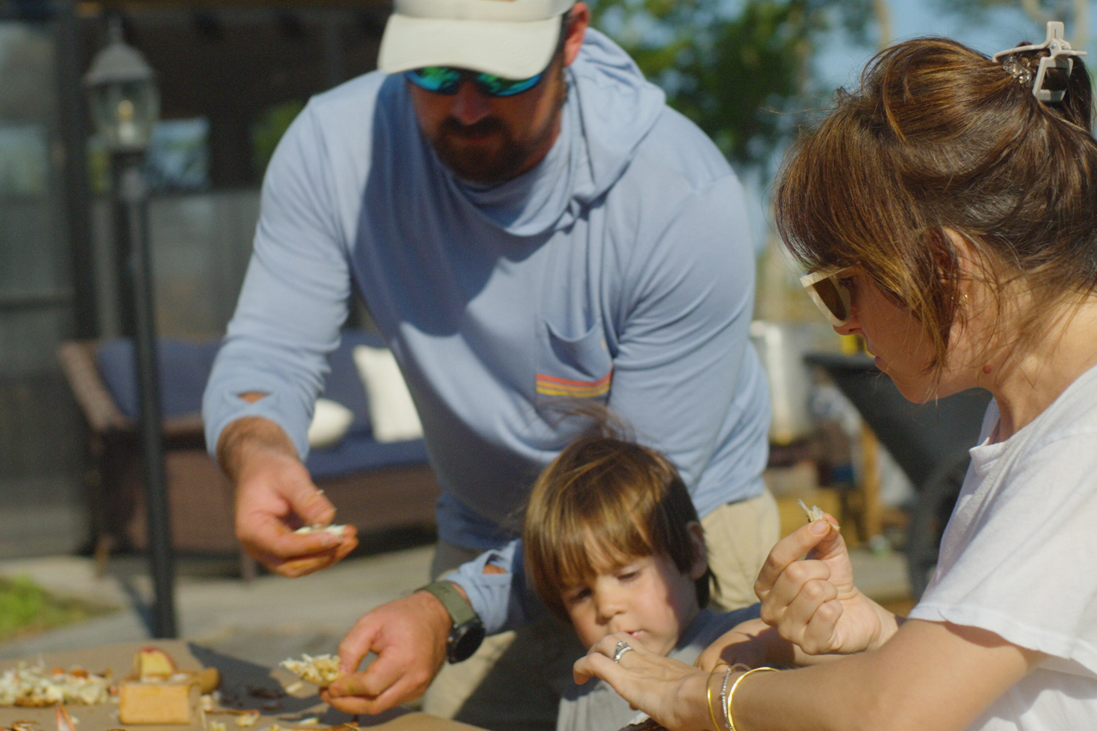 Family with young child shucking oysters together at an outdoor gathering