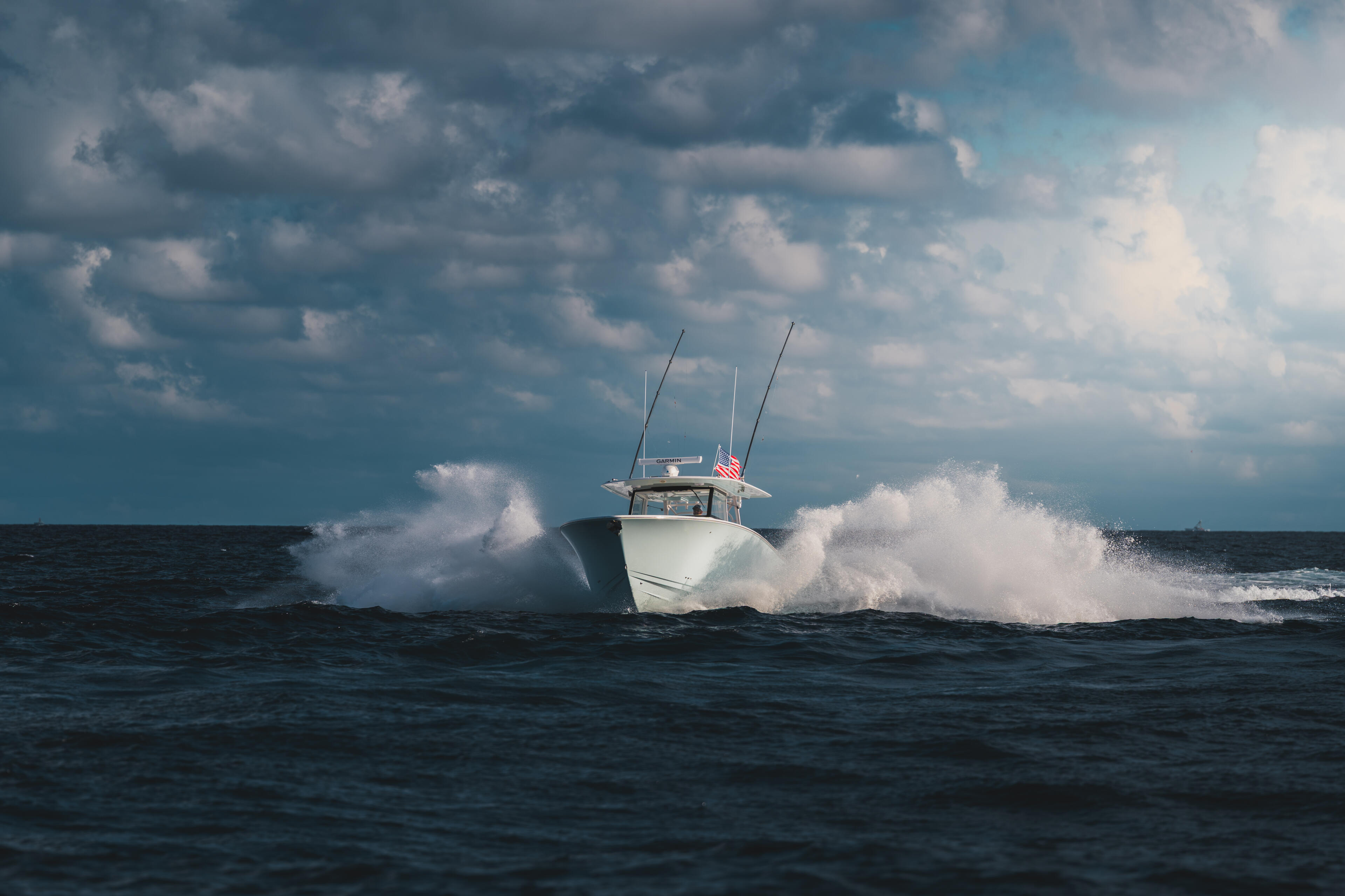 White fishing boat with outriggers running through rough offshore waters under dramatic cloudy sky