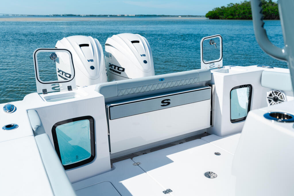 Helm station of a center console boat with dual outboard engines and storage compartment overlooking shallow turquoise water