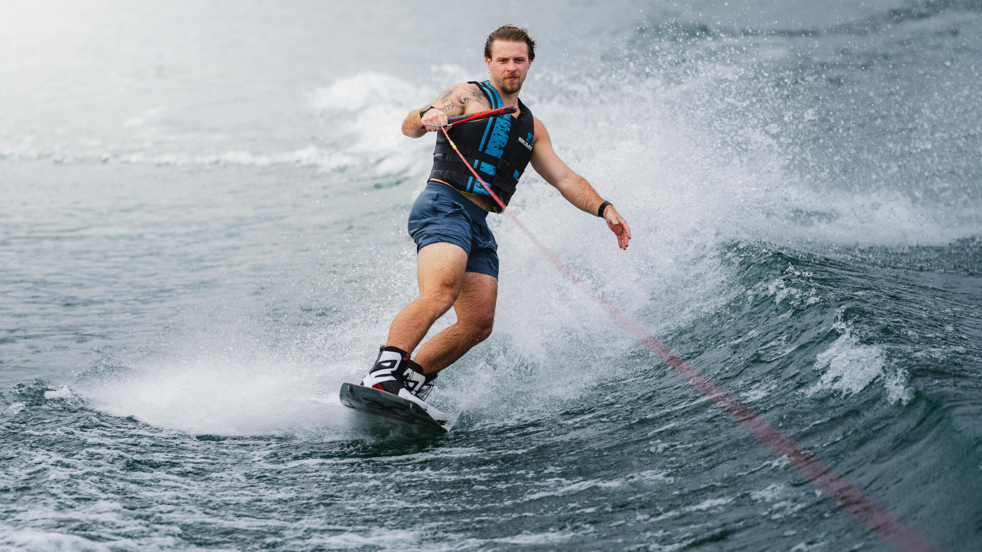 Man wakeboarding behind a boat, holding the tow rope while riding across the wake