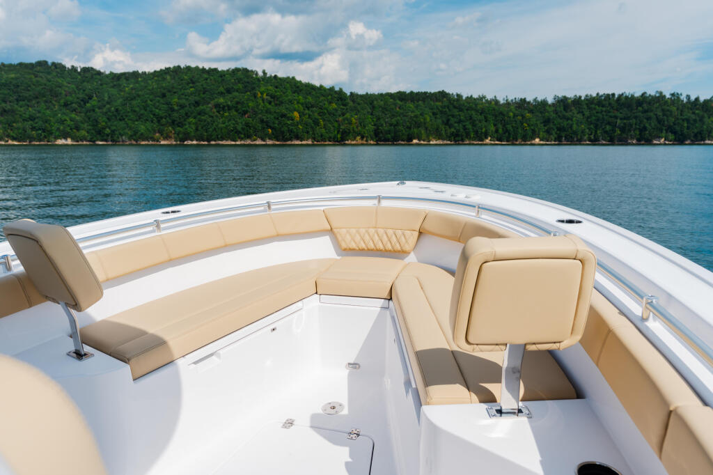 Spacious boat deck with tan wraparound seating facing a forested shoreline and calm lake waters