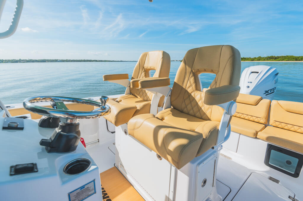 Helm seating area with tan leather captain's chairs, steering wheel, and electronics on calm blue water