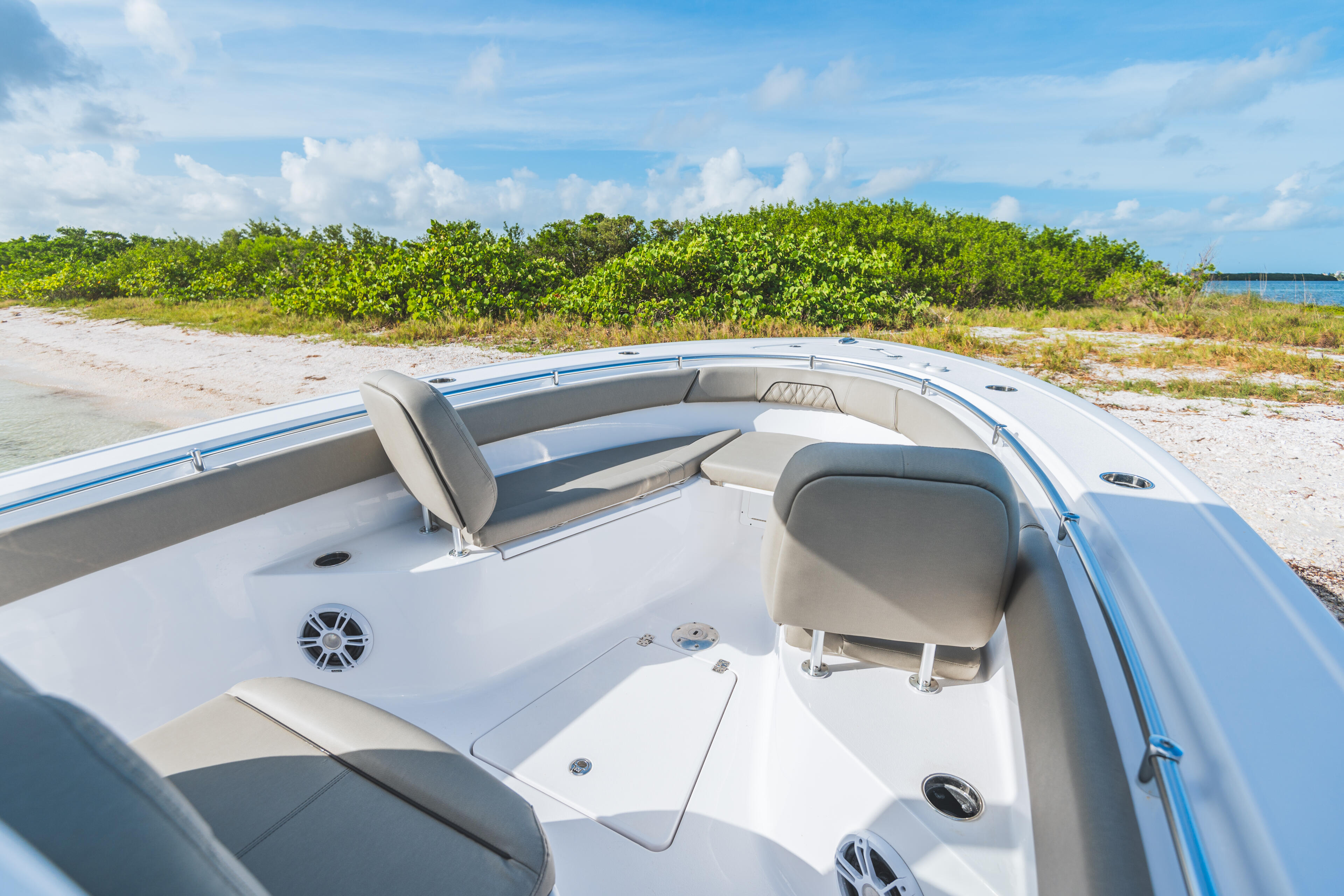 Open center console boat with tan upholstered seating beached near mangroves and shallow water