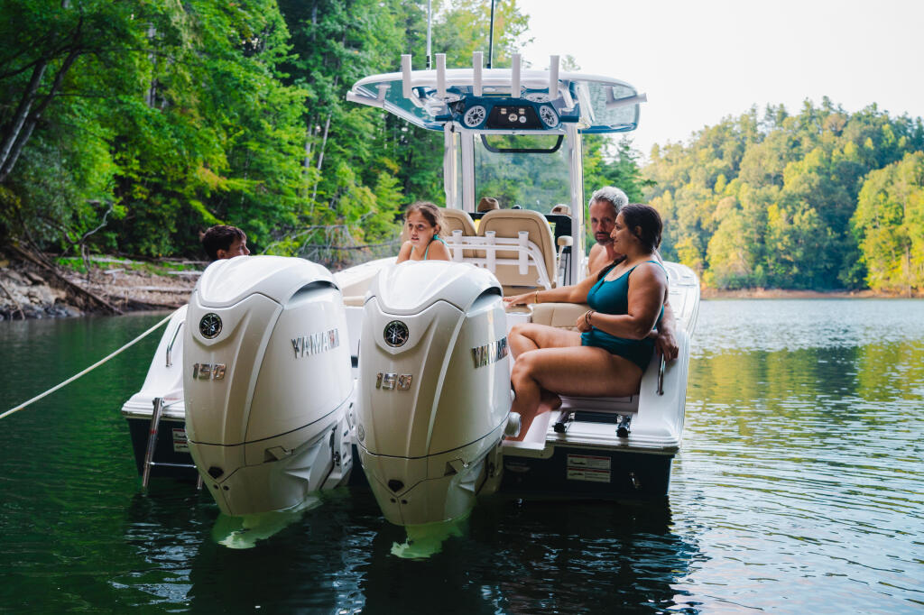 Family enjoying a day on the water in a boat with dual outboard engines, surrounded by forested shoreline