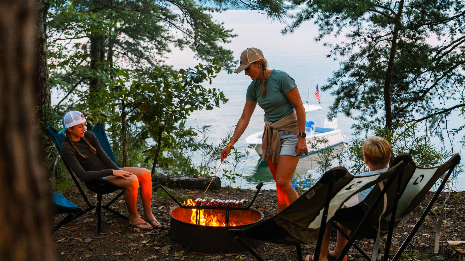Family gathered around a fire pit on a sandbar with boats anchored in the water nearby