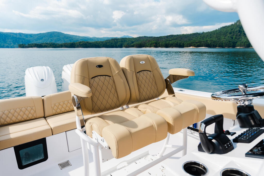 Tan quilted seating and helm controls on a boat with mountain-forested shoreline and blue water in background