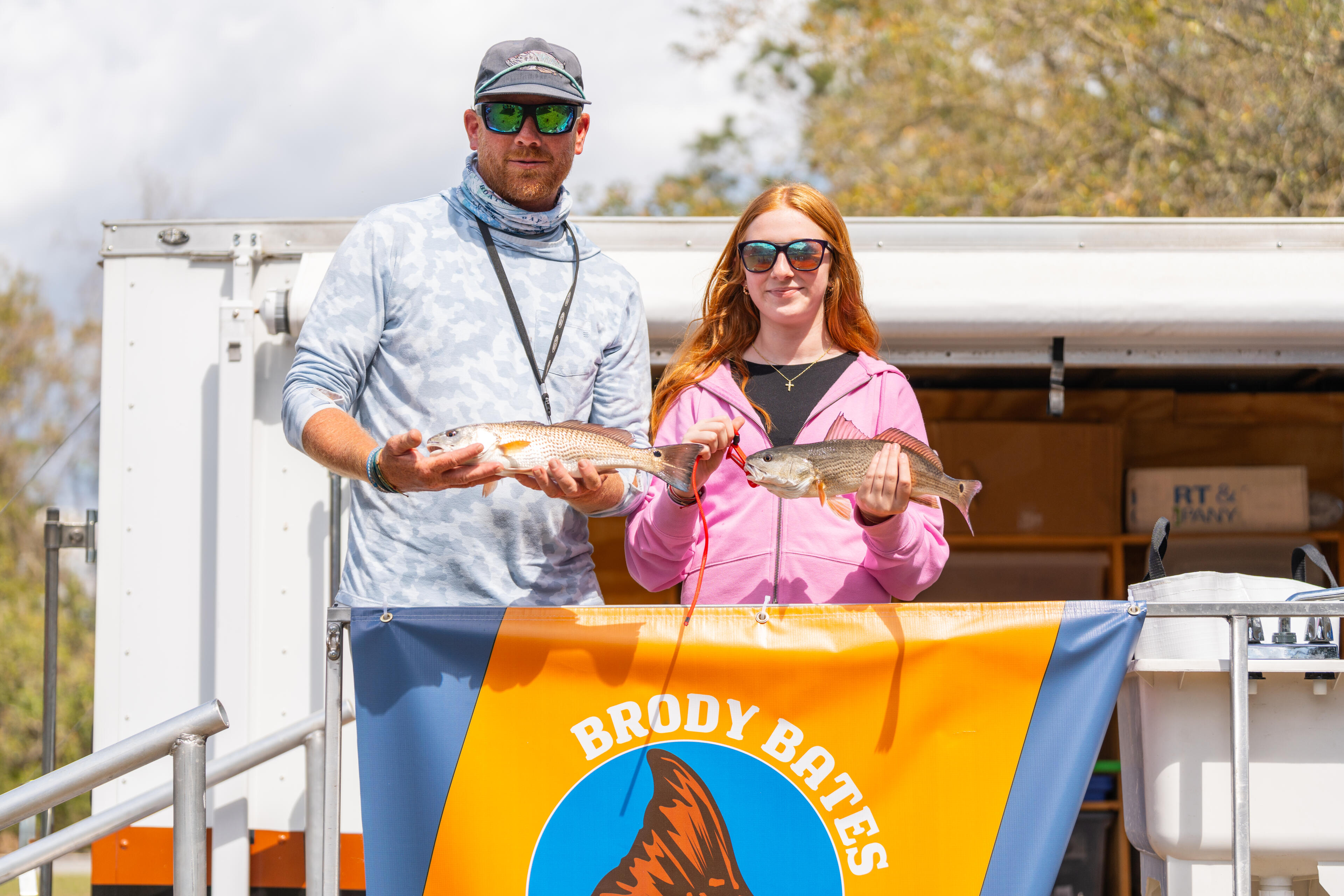 Man and woman display their catch while standing at the helm of a fishing boat