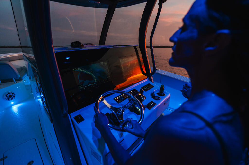 Captain at the helm during sunset cruise with illuminated electronics and calm waters ahead