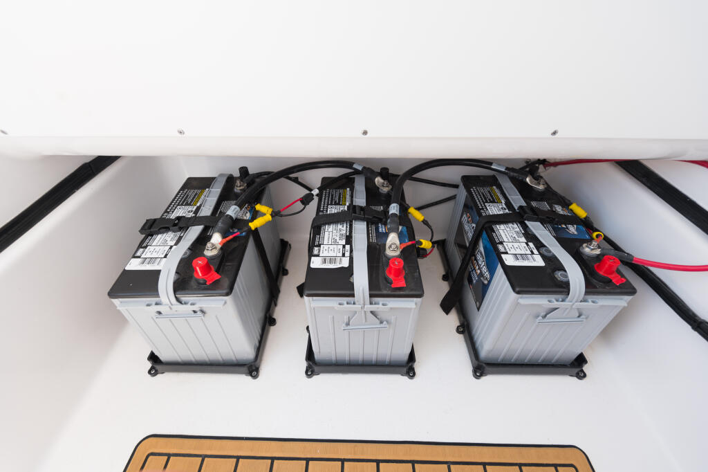 Three marine batteries with red terminals and black cables connected in dedicated storage compartment