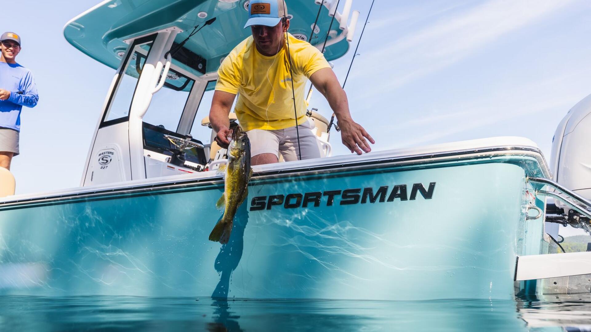 Angler in yellow shirt holds up a freshly caught fish over the turquoise gunwale of a Sportsman boat