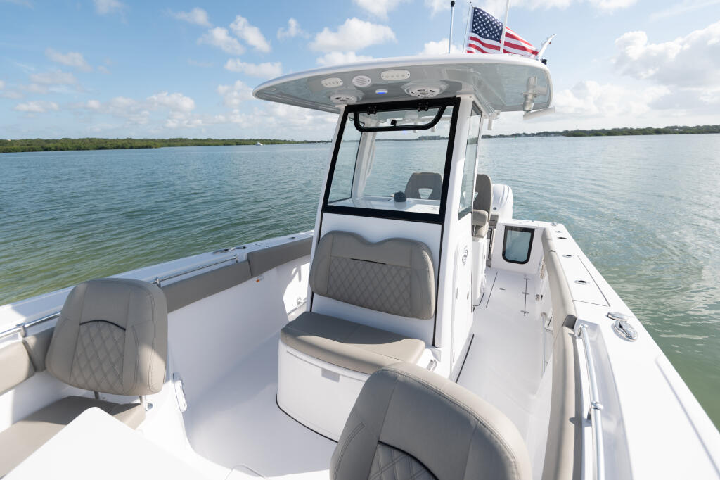 White center console boat with hard-top and gray upholstered seating anchored in shallow turquoise water