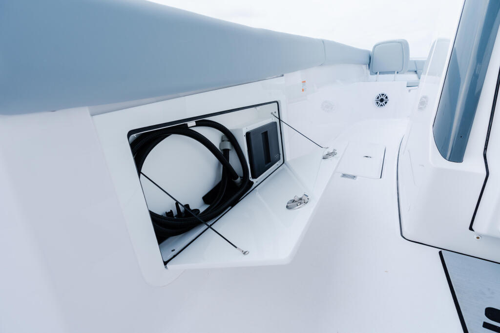 Open hatch on white boat deck showing coiled black hose and storage compartment with hardware details