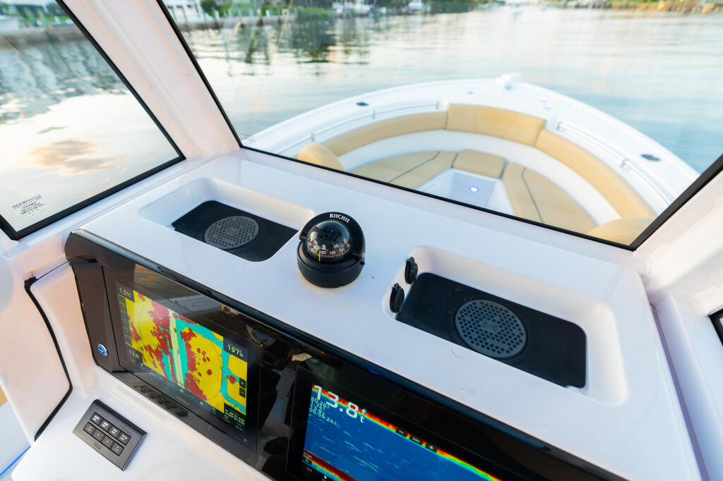 Center console helm with fish finder displays, compass, and speakers overlooking calm marina waters