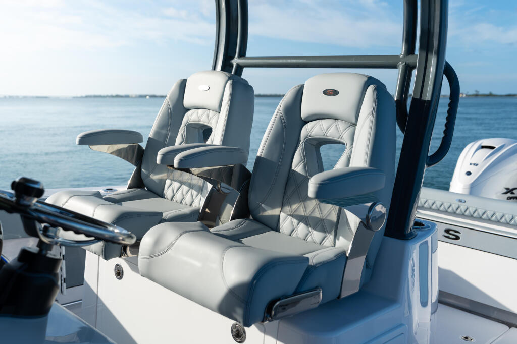 Dual cream and gray quilted helm seats with armrests on center console boat facing calm blue water