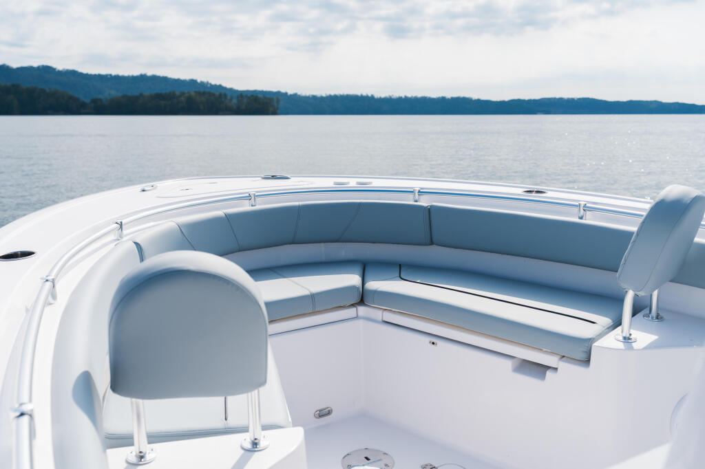 Spacious bow seating area with curved upholstered benches on a white center console boat on calm lake