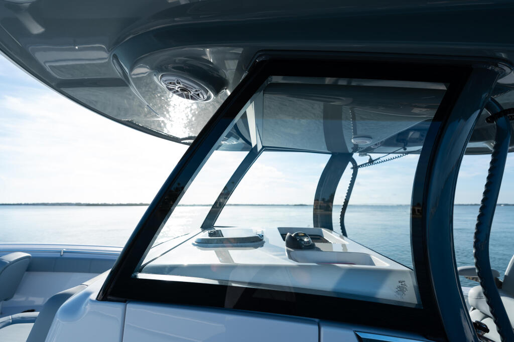 View through boat's windshield and hard-top showing helm with controls and calm water ahead