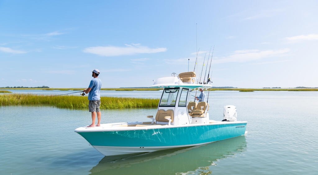 Angler standing on turquoise bay boat equipped with fishing rods in shallow coastal waters