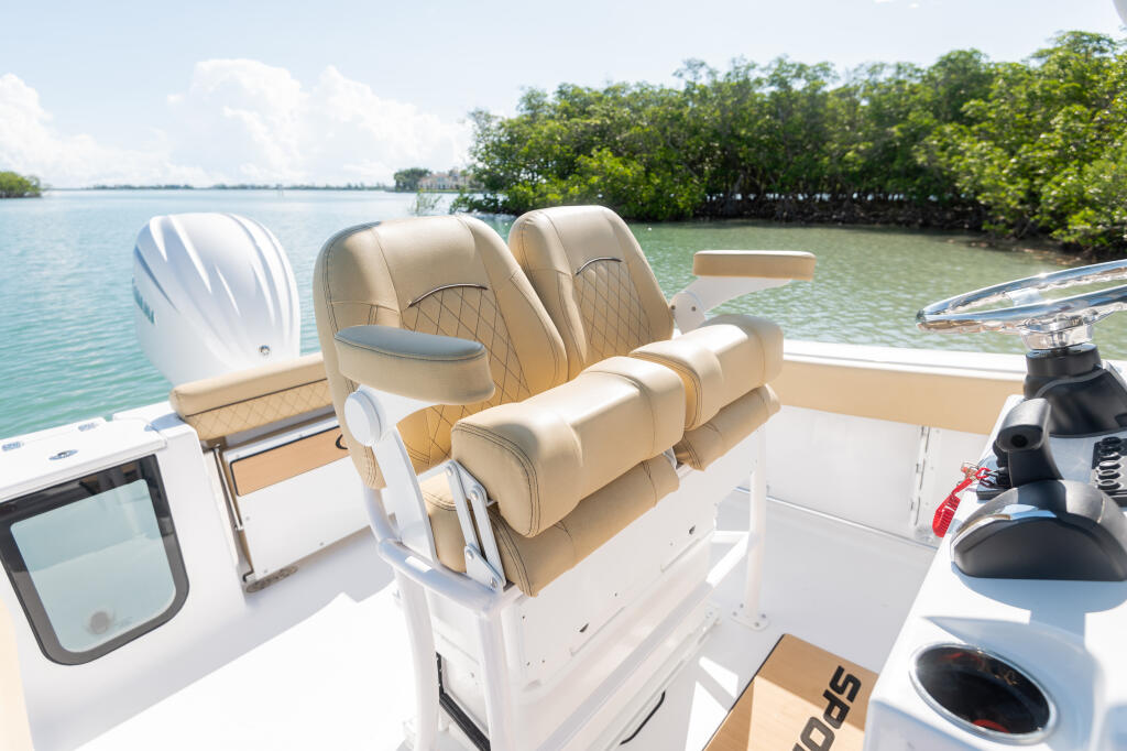 Tan leather dual captain chairs with flip-up bolsters on center console boat facing mangroves and clear water